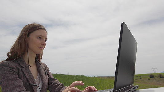 忙碌的妇女带着耳机和笔记本电脑独自在绿色的田野里自由自在视频的预览图