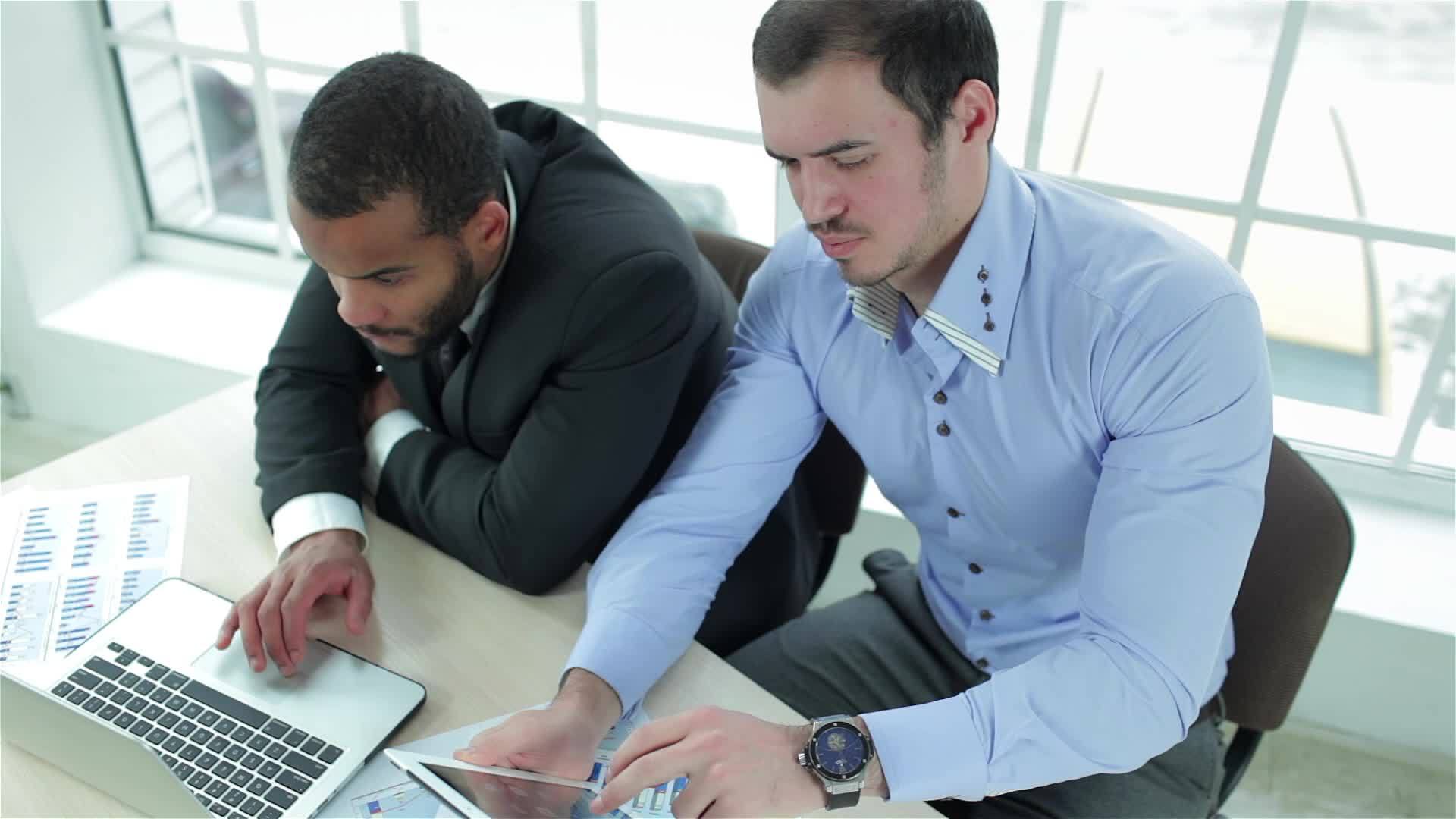 两个严肃的商人在平板电脑和笔记本电脑上工作视频的预览图