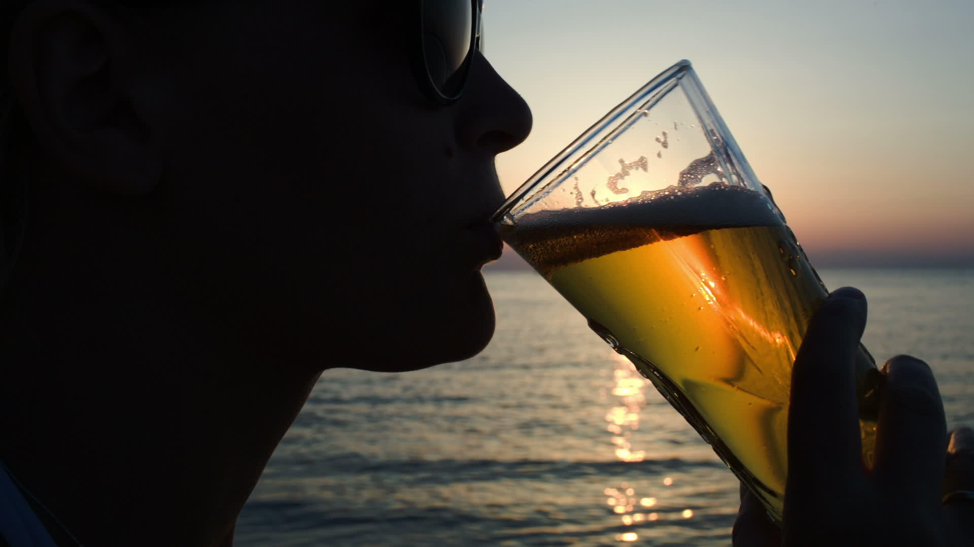 日落时在海滩上喝啤酒的女人视频的预览图