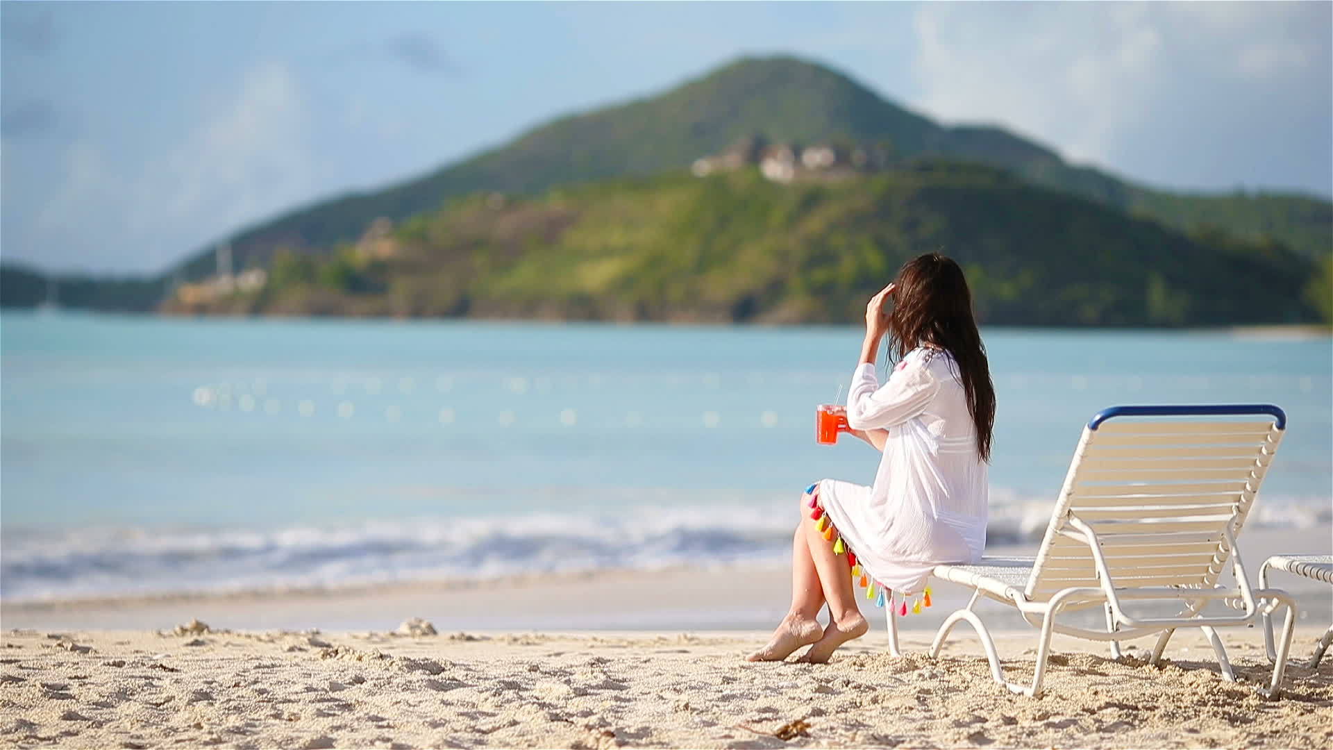 坐在阳光下的年轻女子坐在白色沙滩上的鸡尾酒杯里视频的预览图