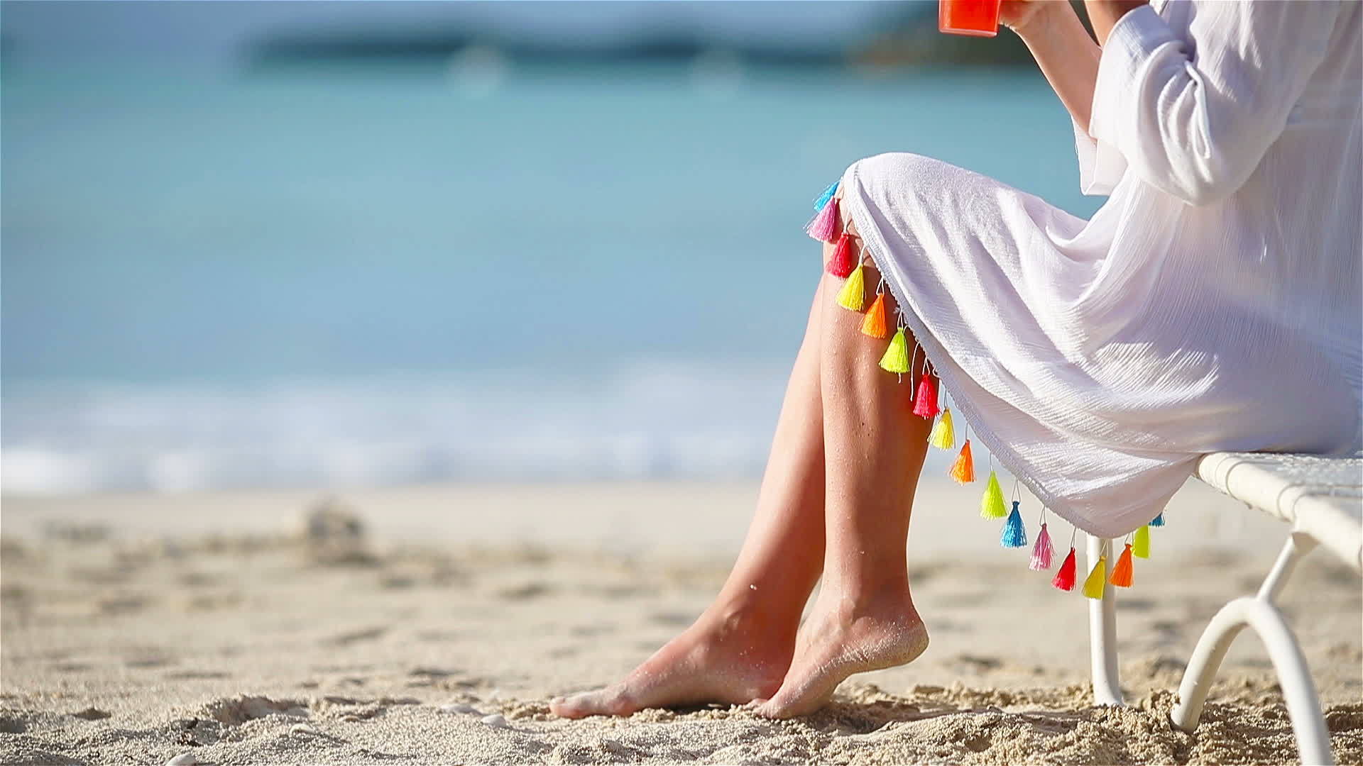 白色海滩上有鸡尾酒杯的年轻女子坐在阳光下闭着美味的鸡尾酒视频的预览图