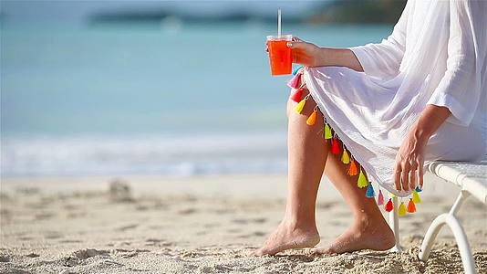 坐在沙滩上的年轻女子坐在阳光下喝着美味的鸡尾酒视频的预览图