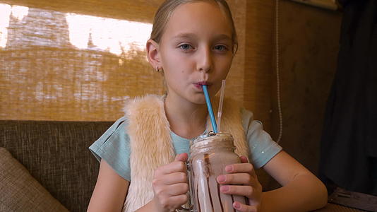 喝奶昔鸡尾酒的十几岁女孩在咖啡馆的餐桌上视频的预览图