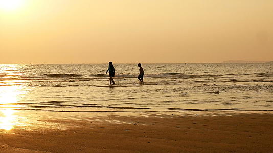 姐姐和哥哥在日落时分在海滩上奔跑和玩水的剪影是美丽和美丽的视频的预览图