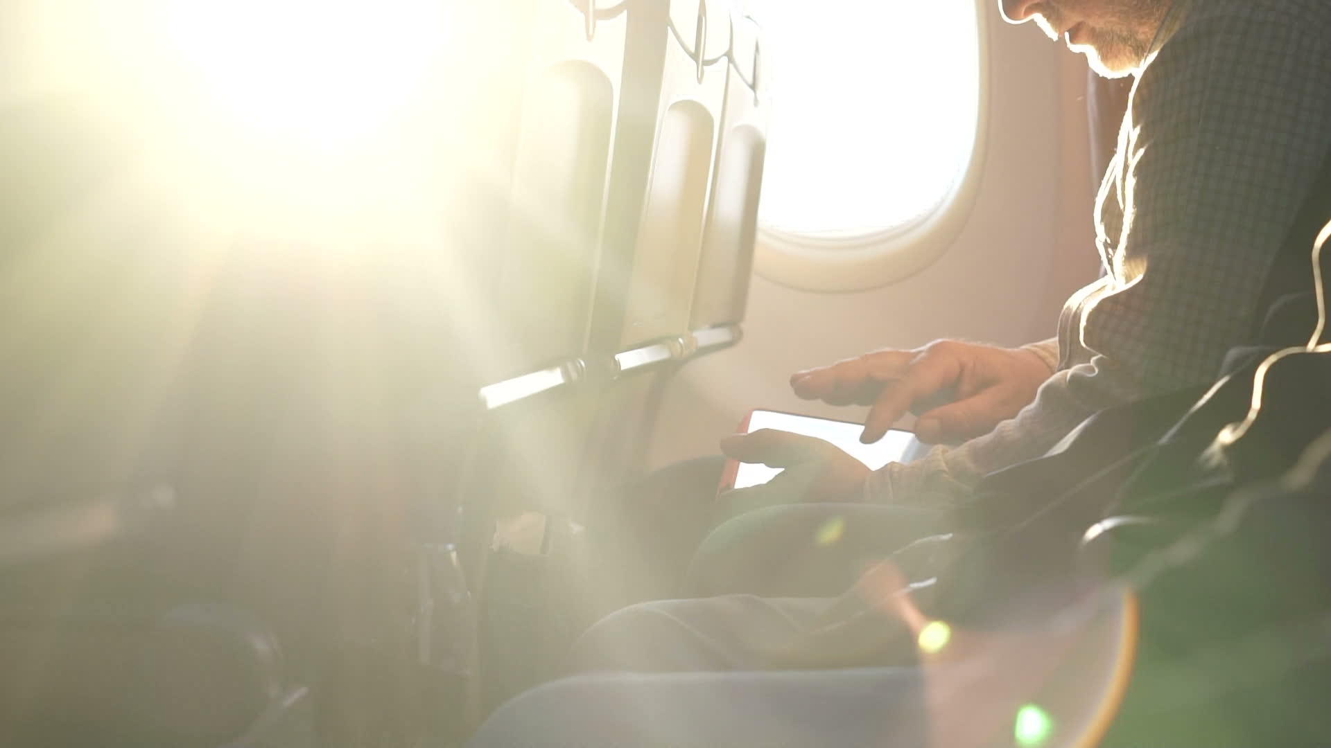 阳光透过飞机窗户照射在一个手持手机的男人身上视频的预览图