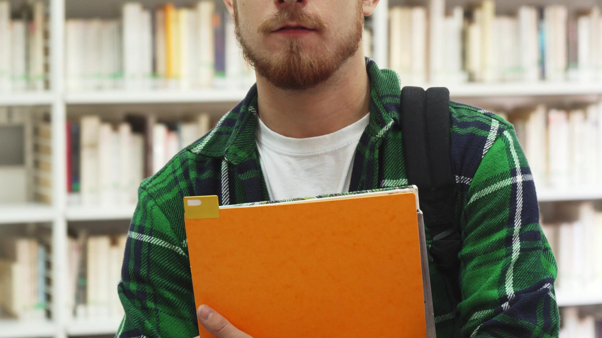 一个拿着教科书的年轻学生站在图书馆里视频的预览图