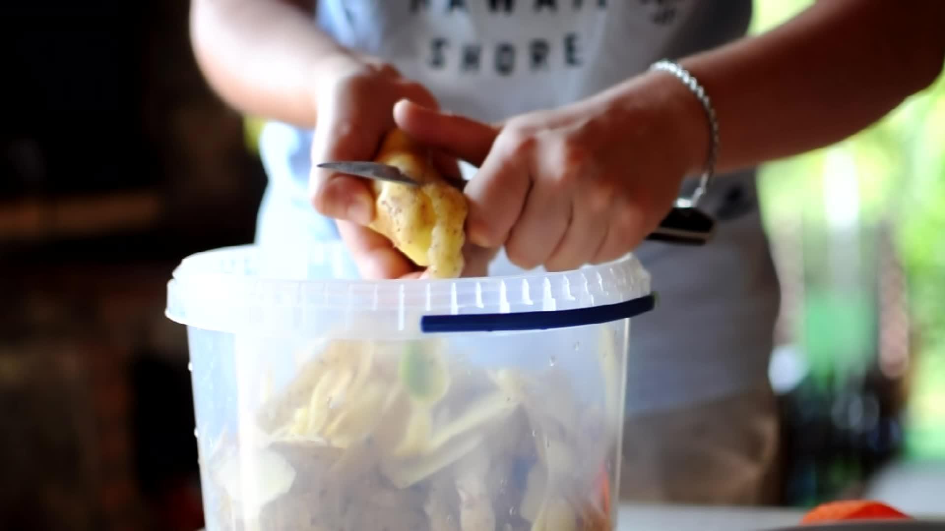 一个女人用刀剥土豆的近视皮从塑料容器上掉了下来视频的预览图