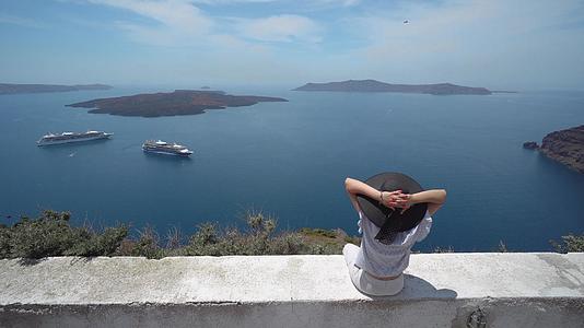 优雅的女士戴着帽子欣赏圣塔里尼岛的美丽风景和火山巡洋舰视频的预览图