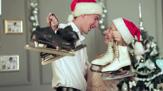 圣诞树前的一对可笑的情侣拿着一双溜冰鞋拥抱着视频的预览图