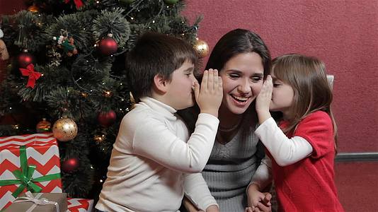 两个孩子在圣诞树前和妈妈耳语视频的预览图