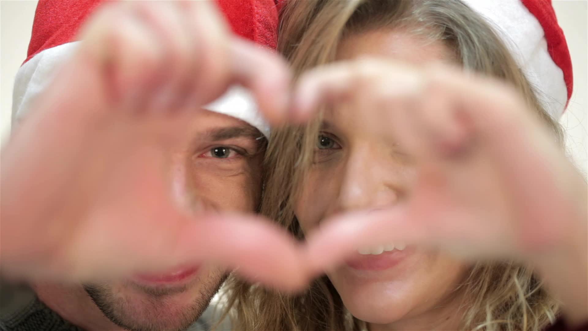 这对戴着圣诞帽的滑稽情侣从手指的心脏窥视着视频的预览图