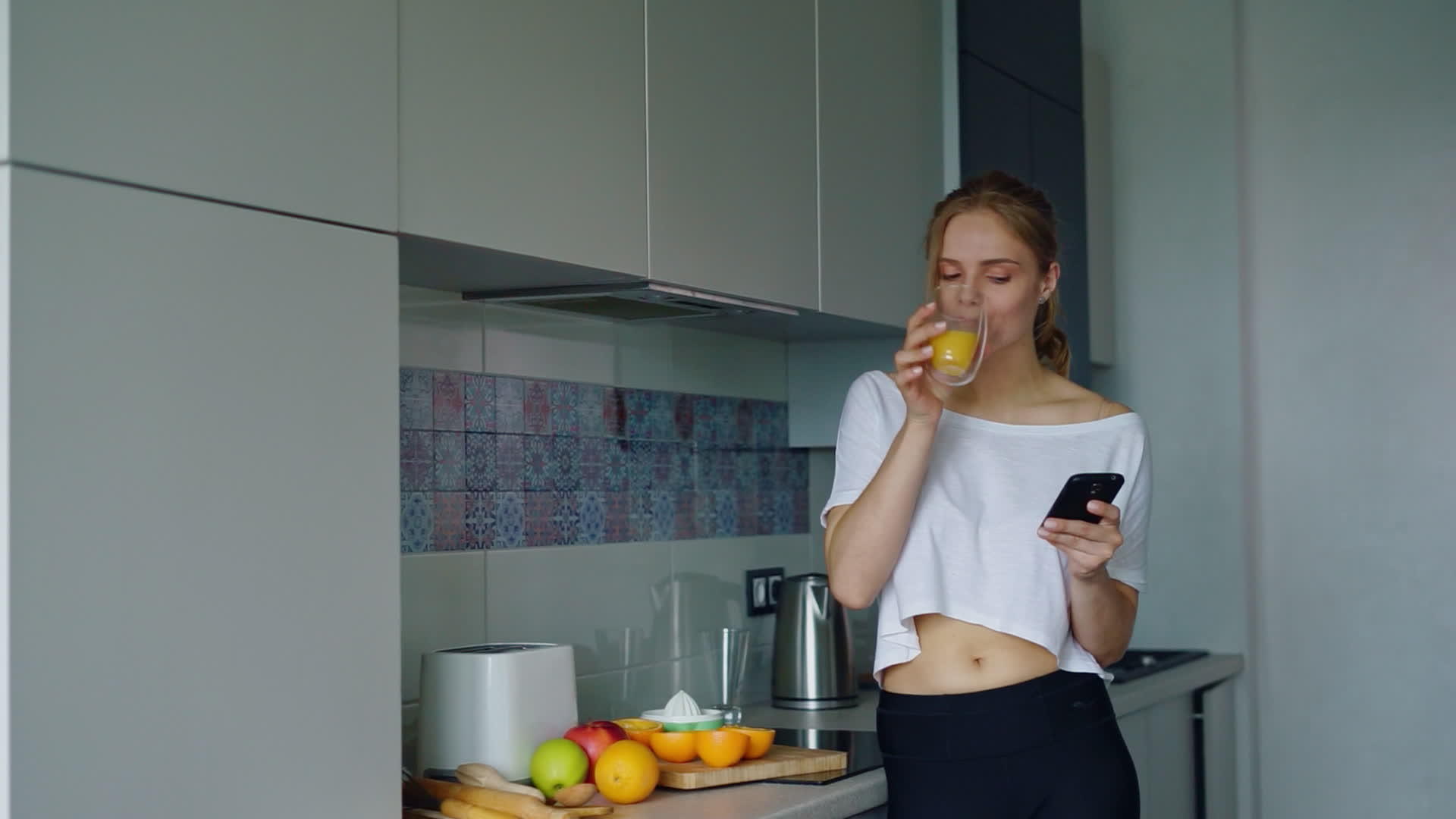 女人用智能手机喝杯子里的新鲜橙汁视频的预览图