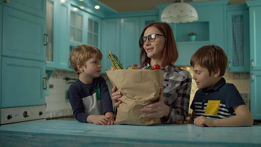 两个孩子帮助30多岁的年轻母亲打开纸袋里面装满了新鲜食物视频的预览图
