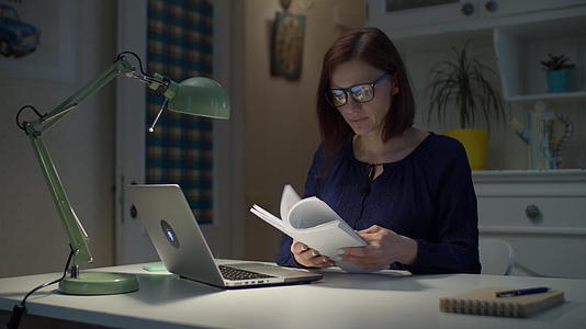 30多岁的年轻女商人在家工作阅读纸质文件和笔记本电脑视频的预览图