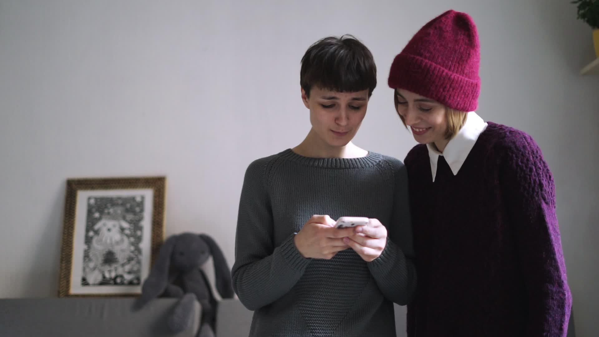 两个穿着时尚毛衣的女人穿着智能手机照片视频的预览图