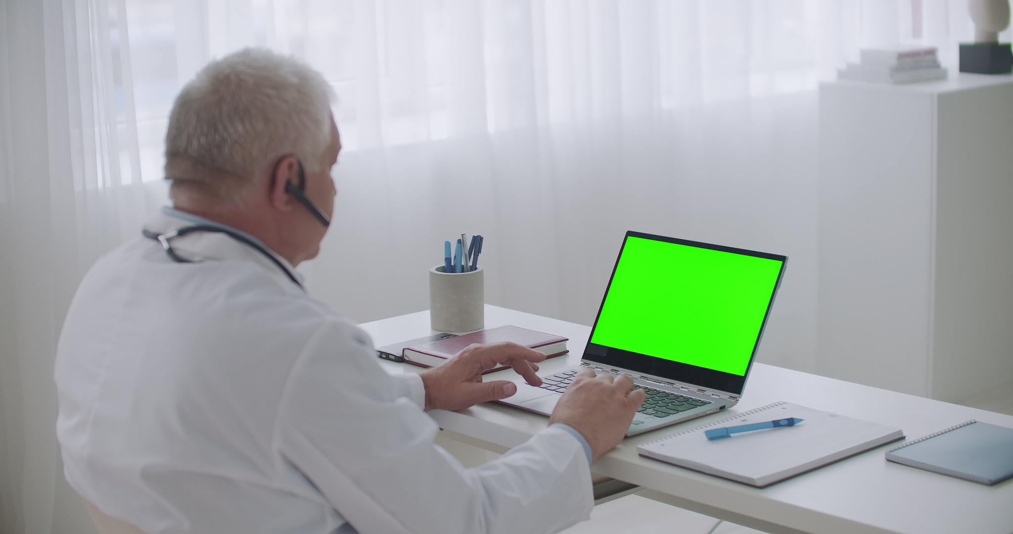男性医生正在用笔记本电脑观看和收听在线研讨会的绿色显示视频的预览图