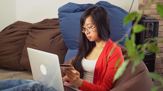 年轻的亚洲女性在网上购买豆袋椅上的电脑视频的预览图