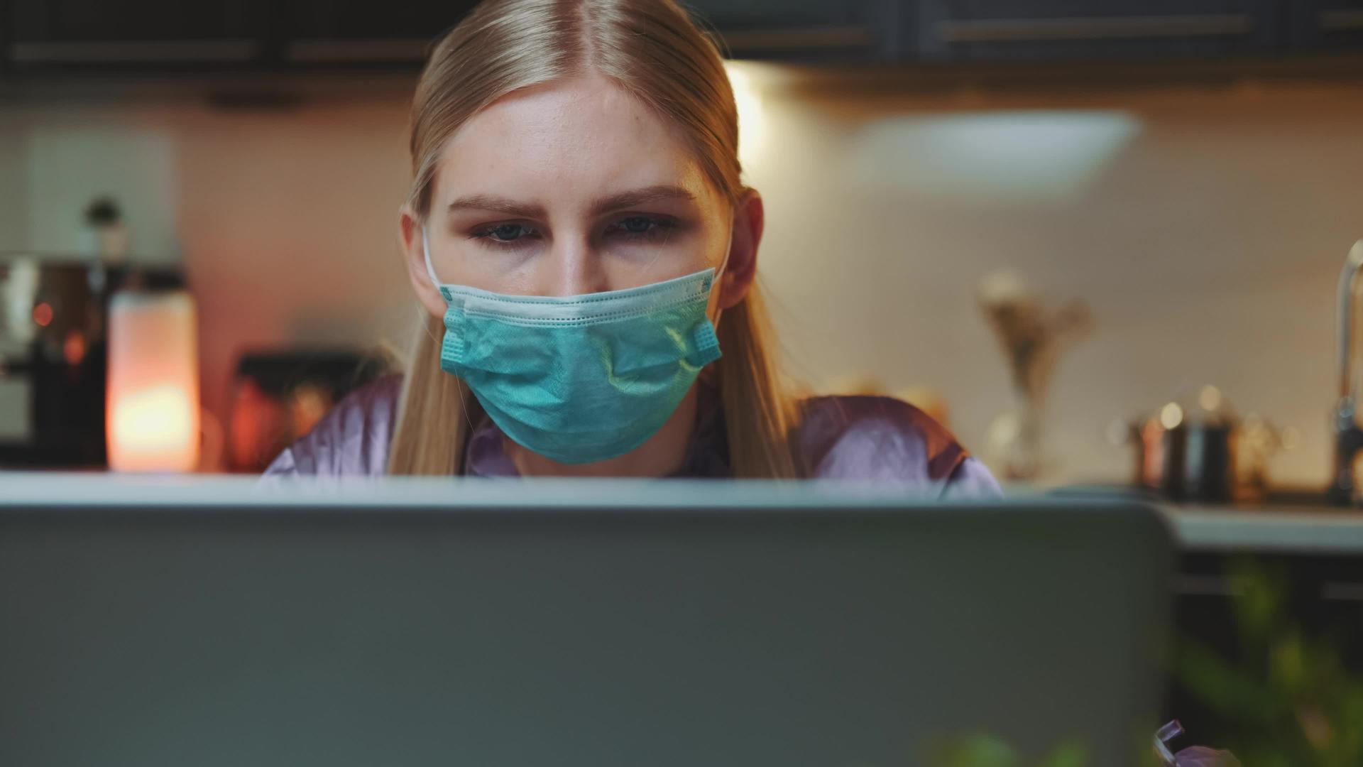 屏幕上戴着中镜头的电脑监视器和戴着医疗面具的女性视频的预览图