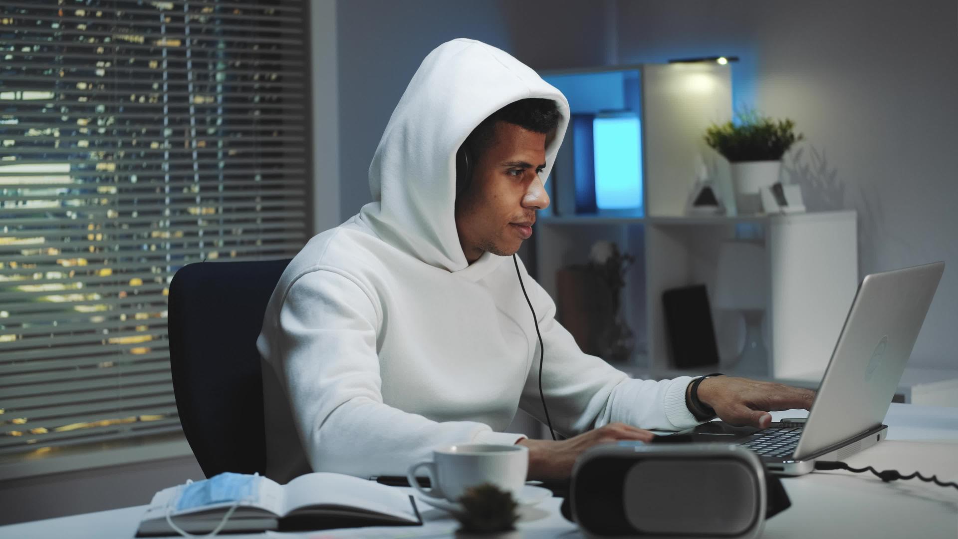 游戏玩家晚上穿着白色连帽衫和耳机在电脑上玩游戏视频的预览图