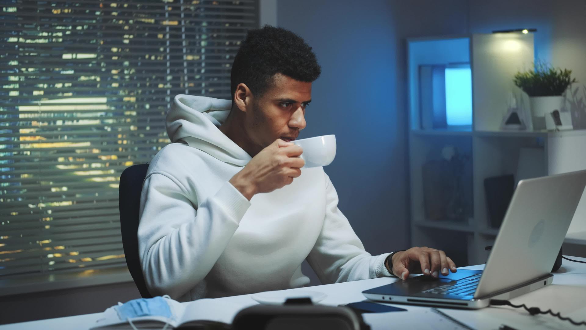 英俊的男人喝咖啡晚上在电脑上工作晚上工作视频的预览图