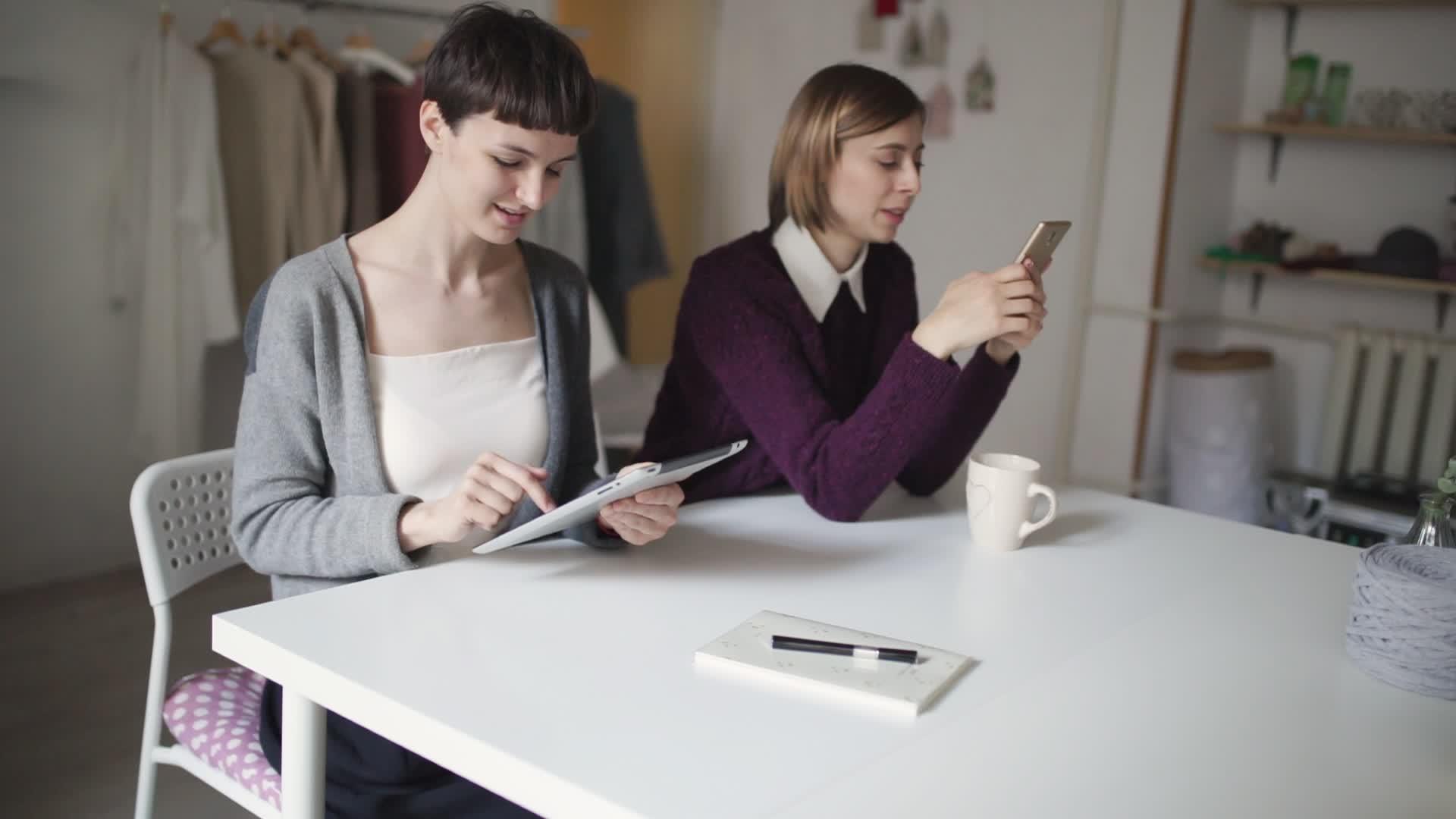 两名女学生用平板电脑和手机坐在桌旁视频的预览图