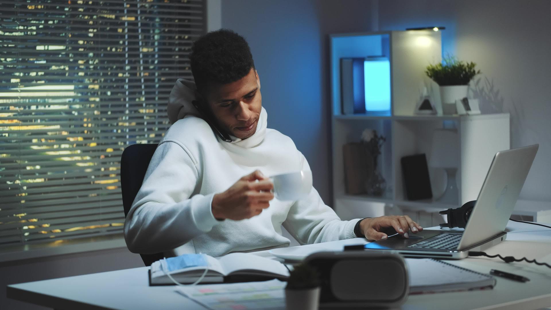 从事计算机工作的混合种族男子用智能手机说话喝一杯茶视频的预览图
