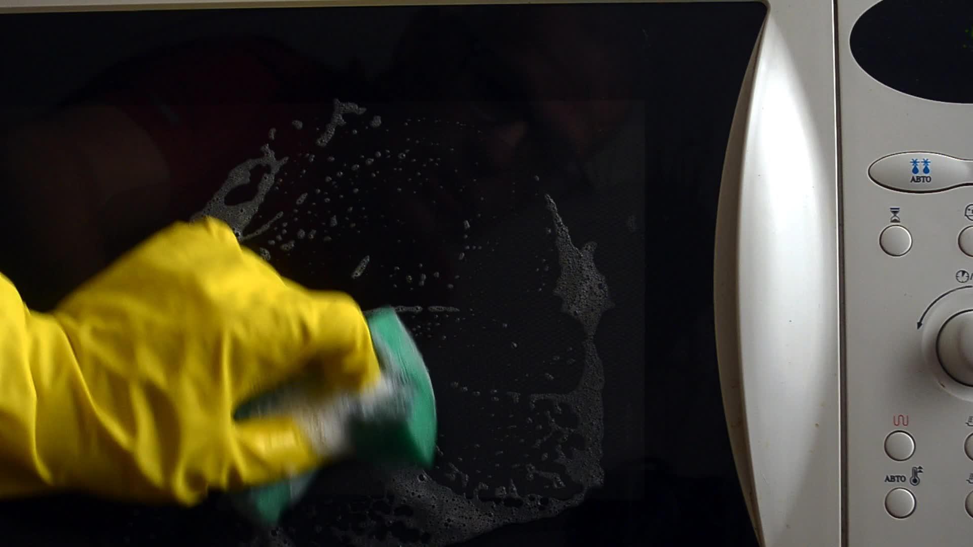 戴防护手套的男子用海绵和溶液清洁微波炉的锁门视频的预览图