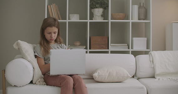 小女孩坐在家里的客厅沙发上用笔记本画画视频的预览图