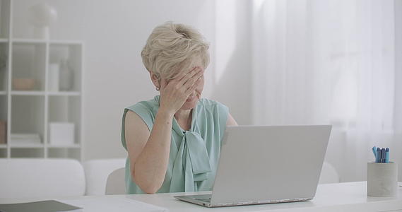 中年妇女在笔记本电脑上工作时头痛视频的预览图
