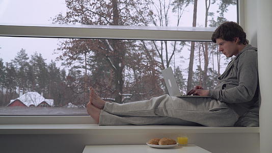 坐在窗台上的男人用笔记本电脑视频的预览图