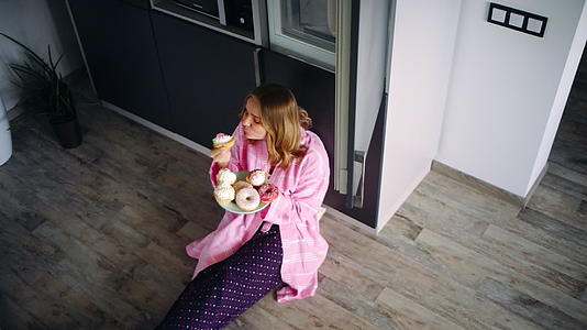 美丽的女人满意地坐在厨房地板上吃甜食视频的预览图