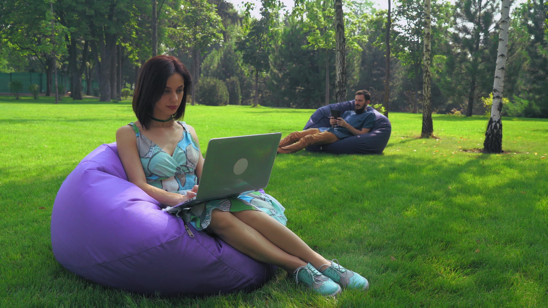 黑发女孩坐在公园懒人沙发上看着笔记本电脑工作视频的预览图