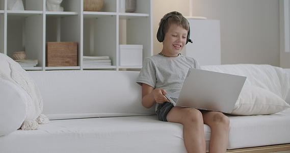 快乐的男孩坐在家里的沙发上通过互联网和一个人愉快地交谈视频的预览图