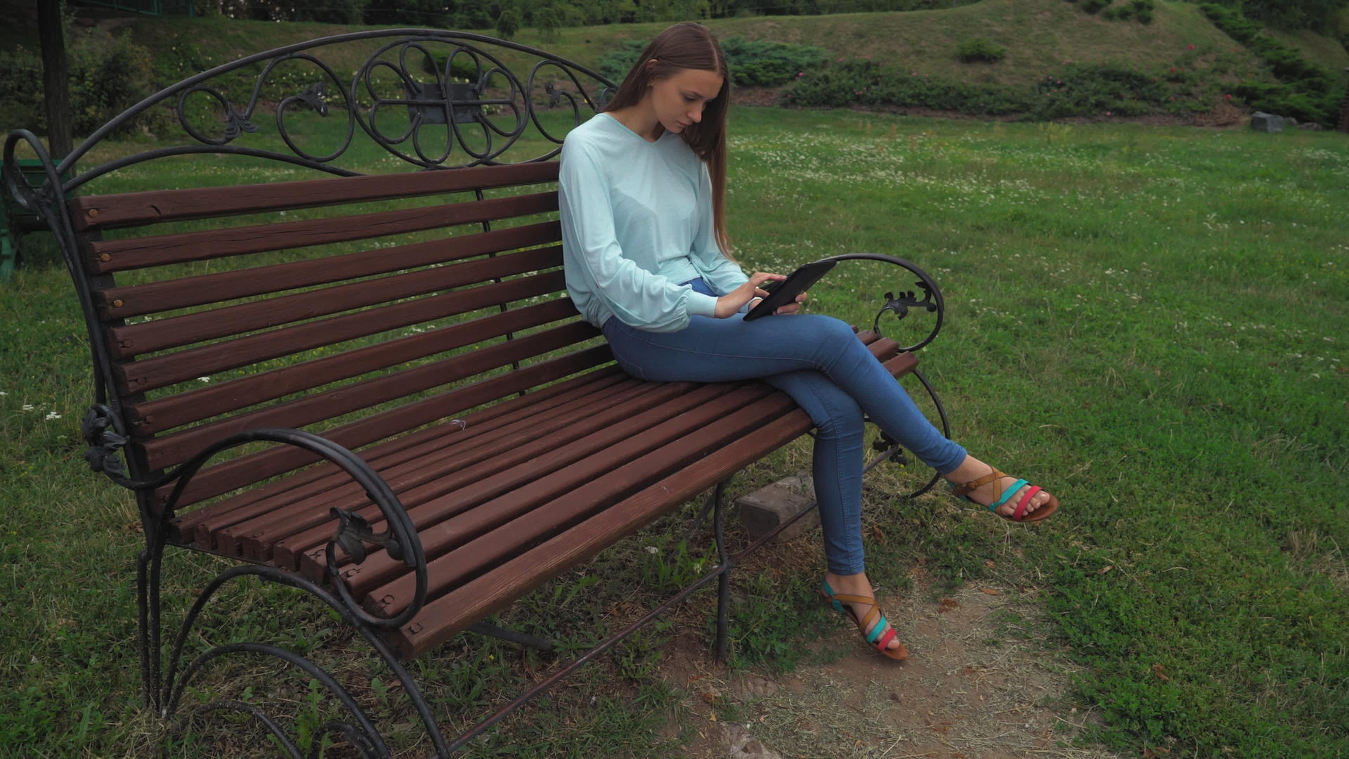 一个年轻女孩坐在公园的长椅上在平板电脑上翻页纸视频的预览图