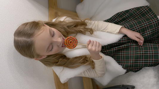 垂直视频在快乐的年轻女孩身上吃糖棒棒糖垂直版视频的预览图