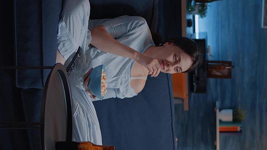 垂直视频放松女性睡衣吃爆米花看电视视频的预览图