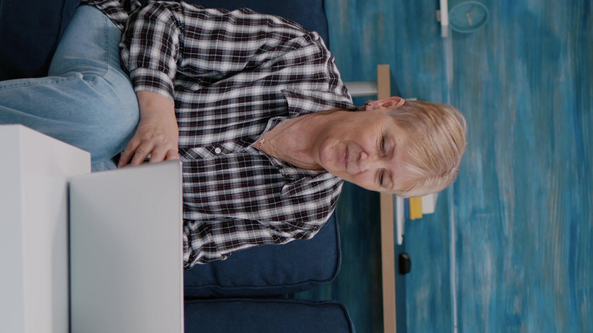 视频通话中双面微笑的老夫妇看着笔记本电脑垂直版视频的预览图