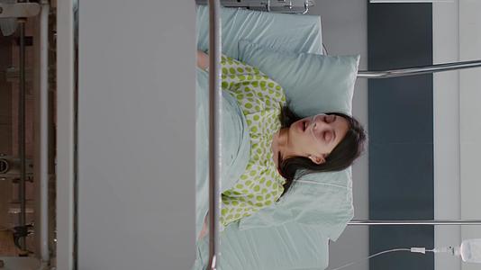 患有垂直视频疾病的成年妇女睡在床上而黑人护士分析疾病视频的预览图