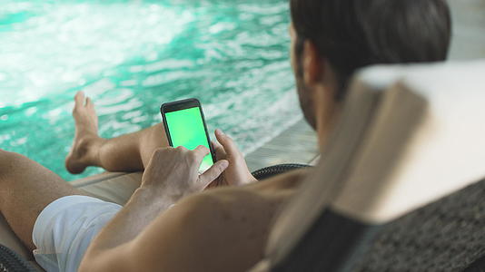 年轻人在手机游泳池边滚动智能机视频的预览图