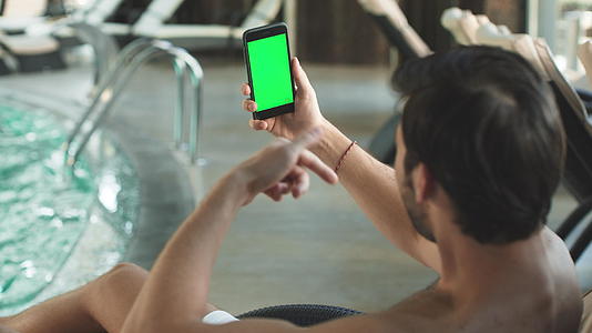 男子在泳池边玩绿屏电话视频视频的预览图