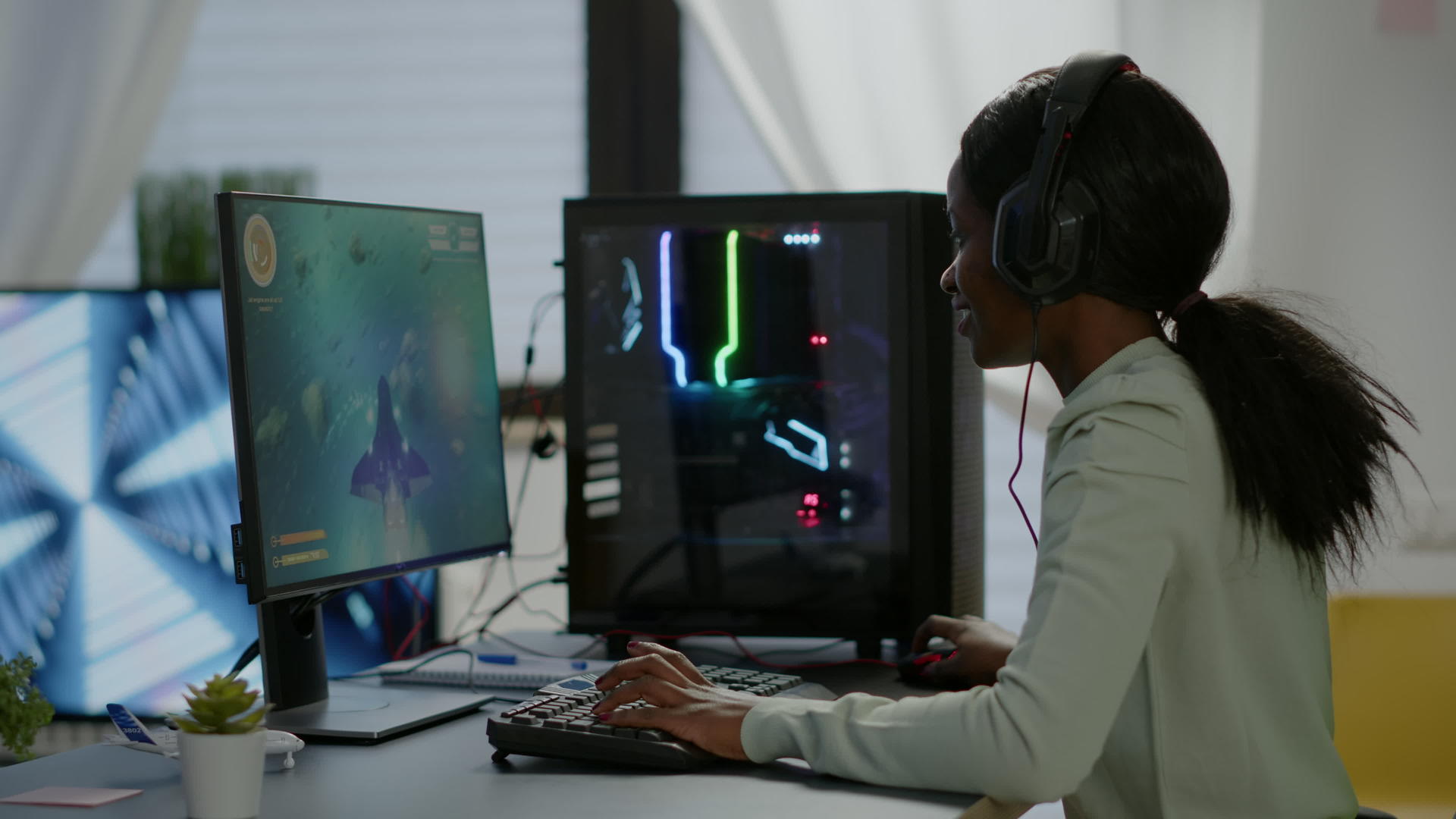 兴奋的黑人女性游戏玩家坐在桌子上戴着耳机玩麦克风视频的预览图