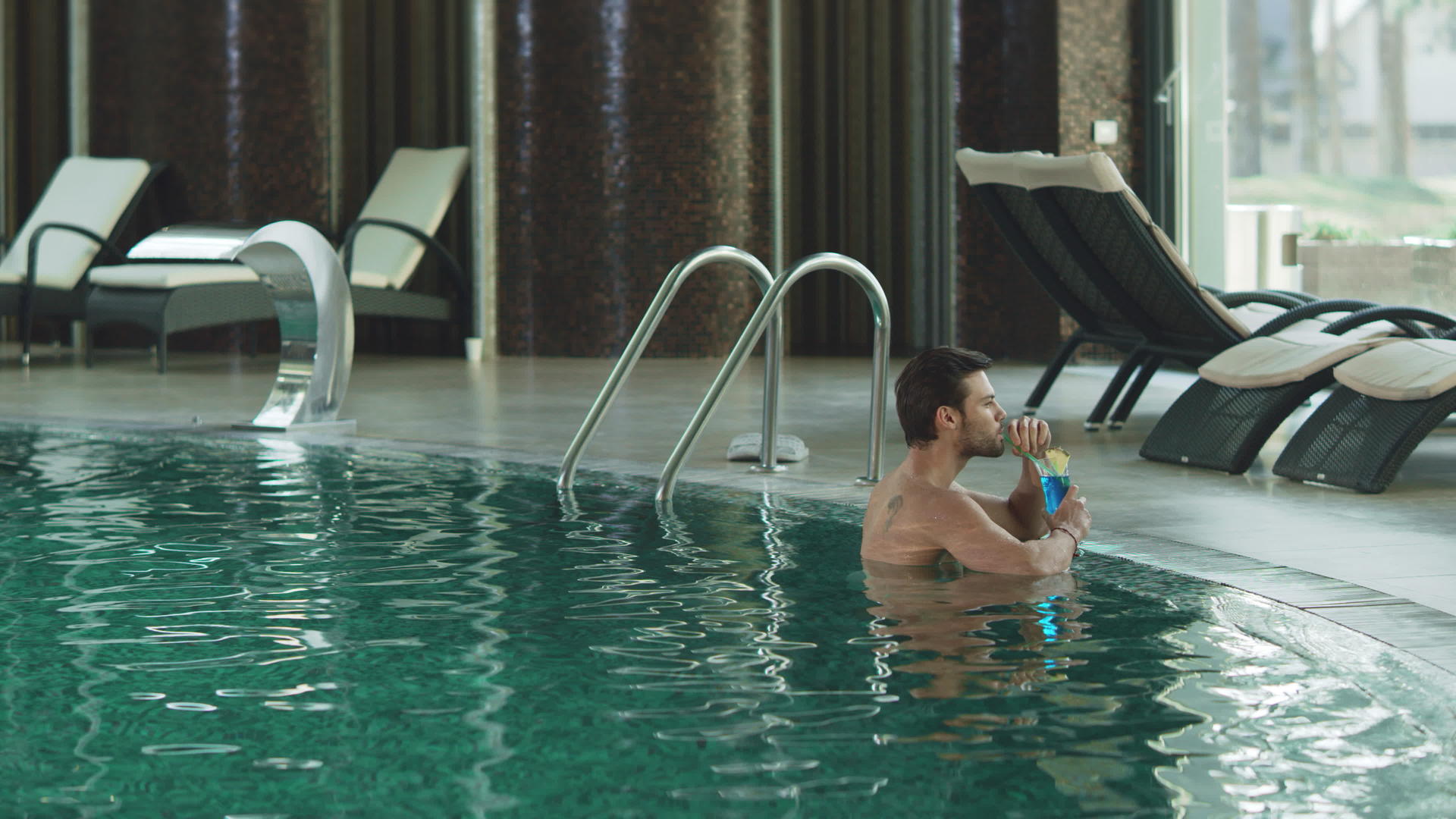 迷人的男人在豪华的游泳池里喝鸡尾酒放松视频的预览图