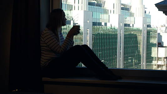 女人在窗台上喝咖啡在窗户上看到城市风景视频的预览图