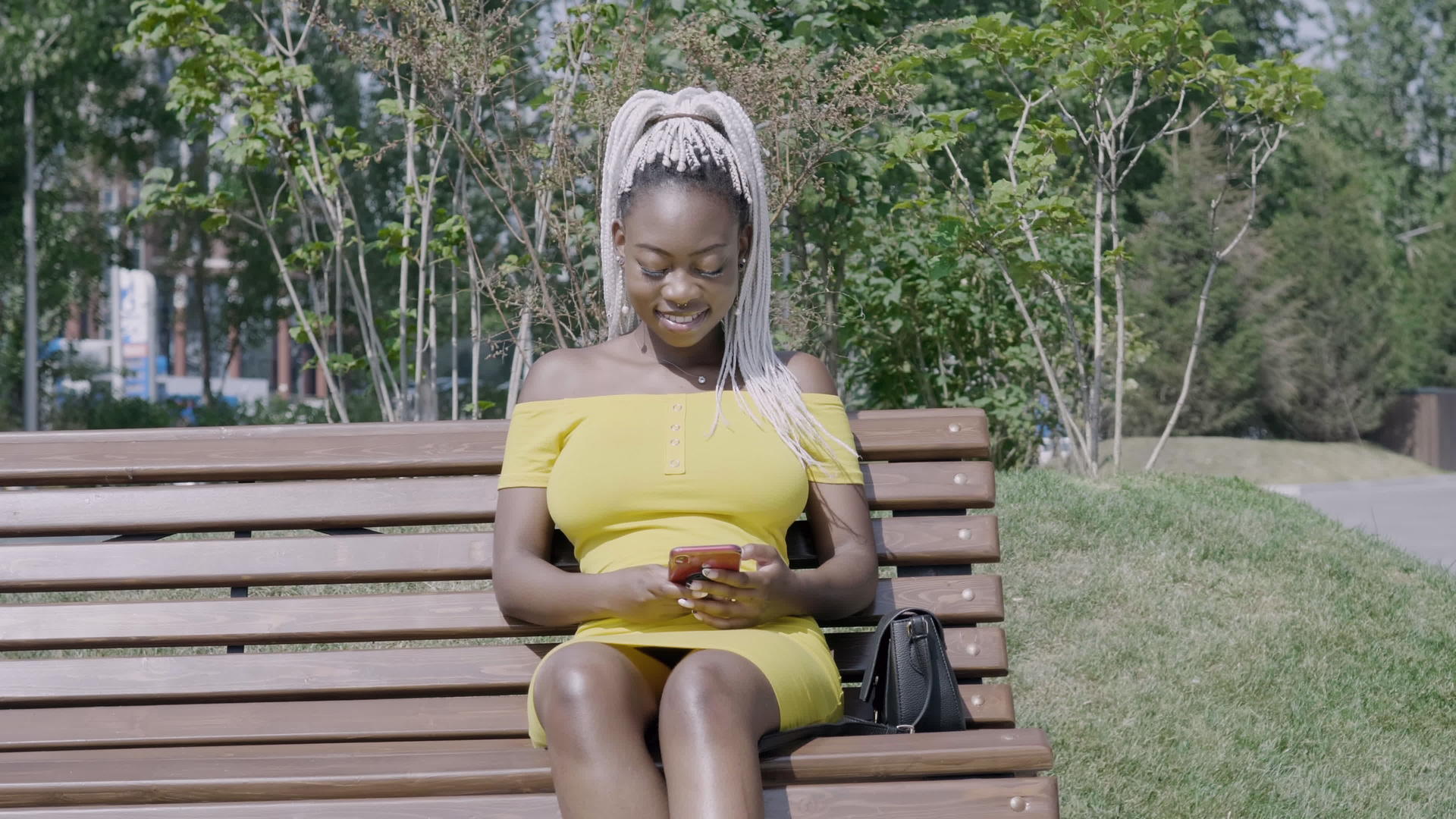 时髦的女孩坐在公园长椅上看手机视频的预览图