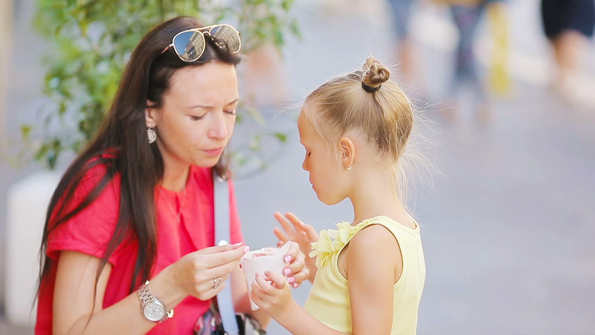 年轻的母亲和女儿在户外吃冰淇淋母亲在街上给女儿喂冰淇淋视频的预览图