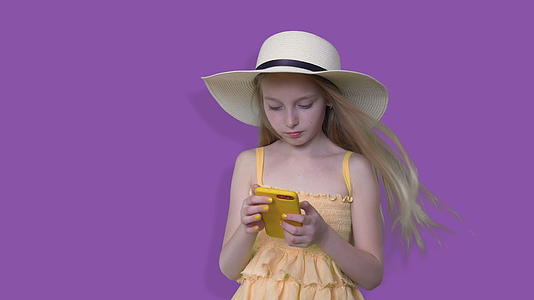 夏天戴帽子的女孩在紫色背景上看手机穿着夏装和帽子视频的预览图