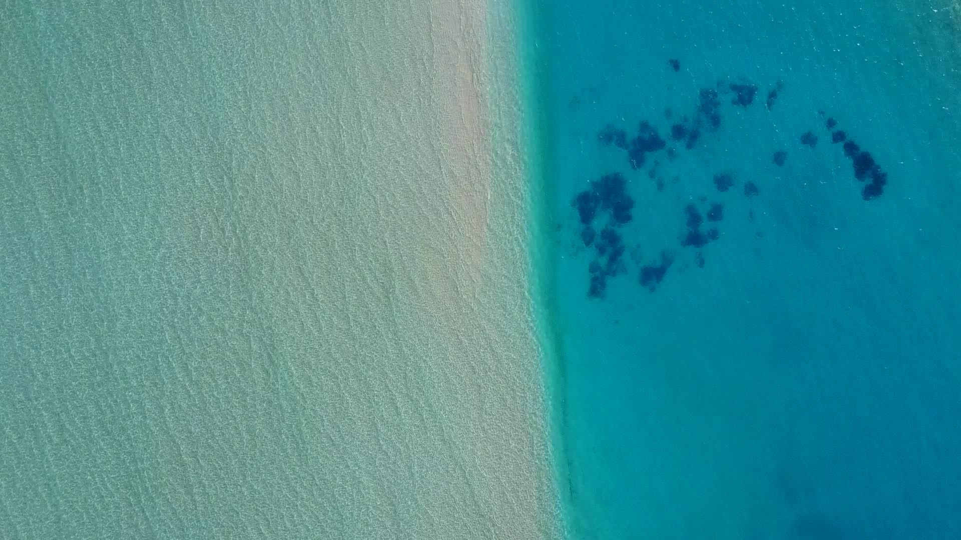 蓝色清澈的海洋在阳光下的白色海滩旁边视频的预览图