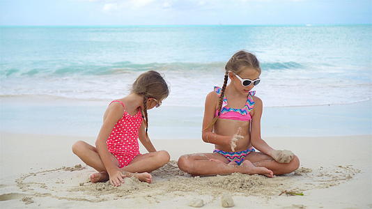 可爱的小女孩在沙滩上玩耍孩子们坐在浅水里做沙堡视频的预览图