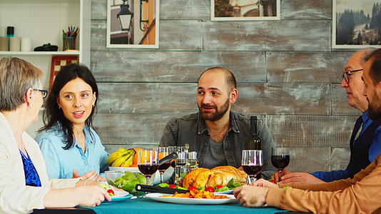 在家吃饭时留着胡子的年轻人用红酒举杯与朋友和家人一起喝红酒视频的预览图