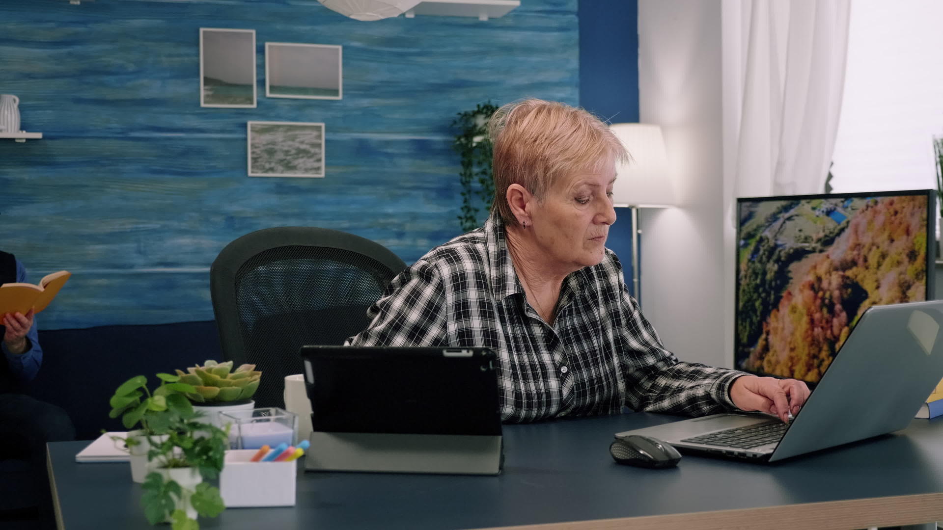 老经理女性在笔记本电脑上打字同时在平板电脑上阅读视频的预览图